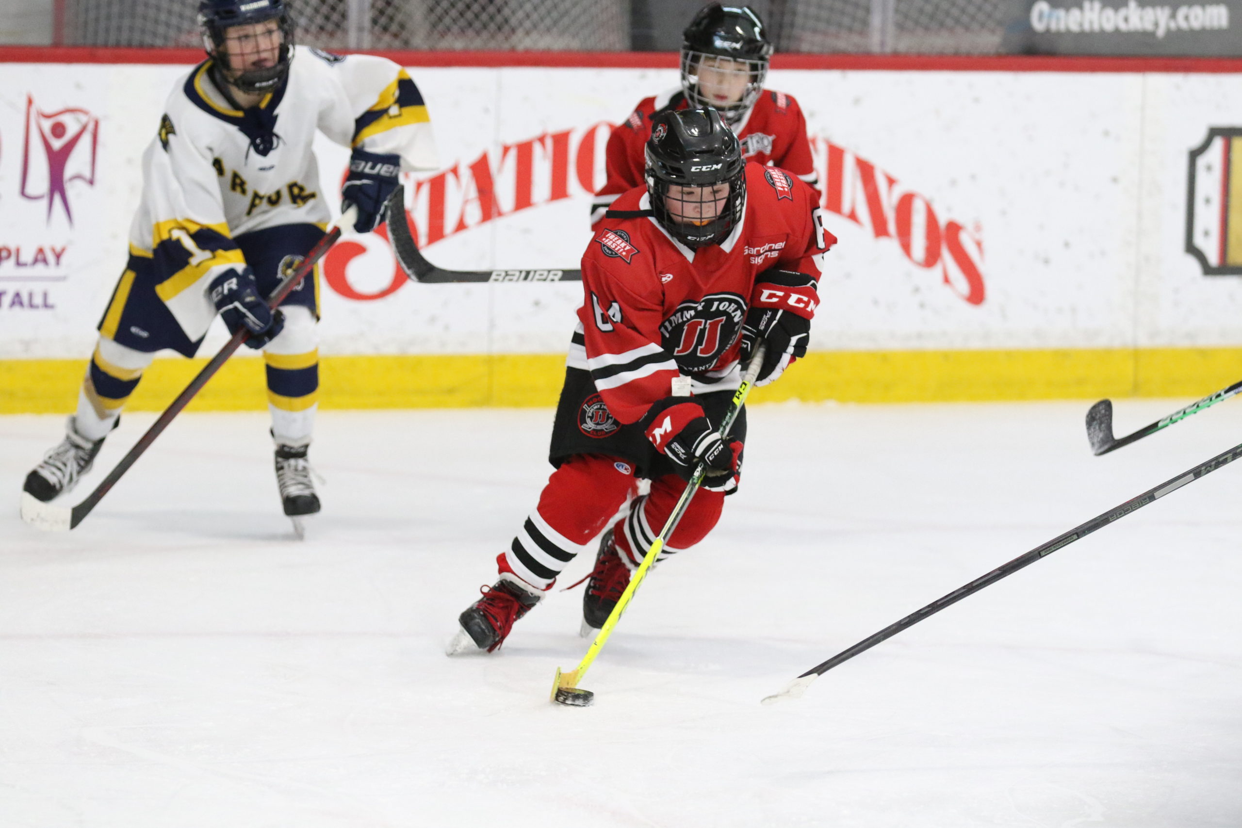 A Jimmy John's hockey player in a red jersey and black shorts stick handles the puck down the ice